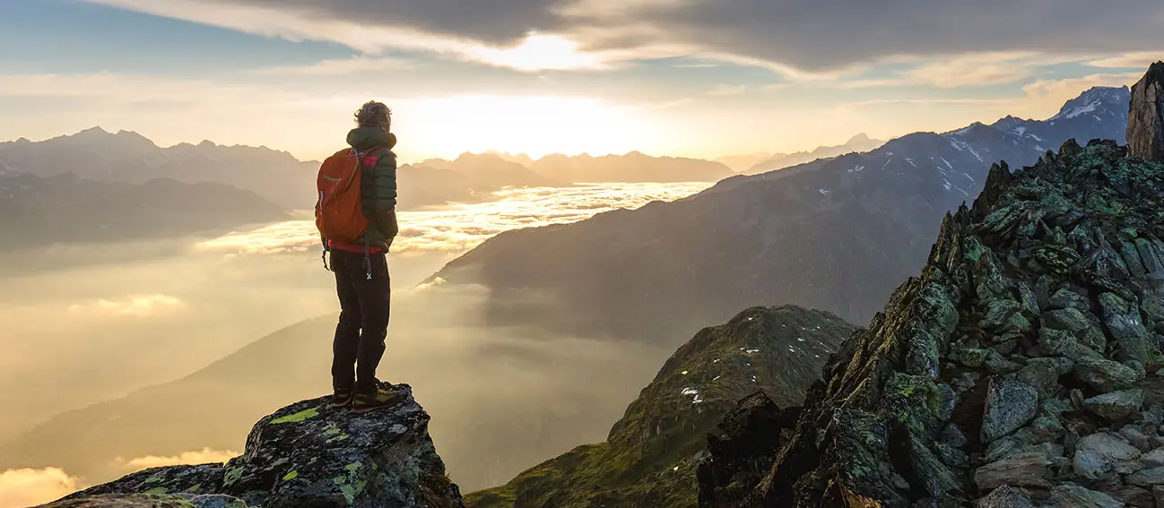 A man standing on a mountain top watching the sun set